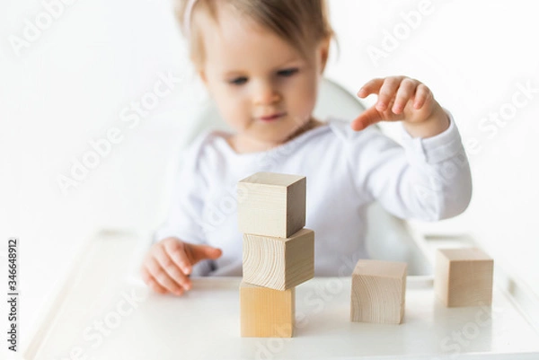 Fototapeta Cute baby girl playing with wooden cubes. Little child building tower. Construction block for kids. Montessori educational method. Selective focus