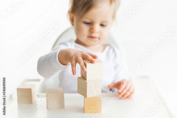 Fototapeta Baby girl playing with wooden cubes by left hand. Playing toddler isolated on white background. Games for kids, preschool education. Close up, selective focus