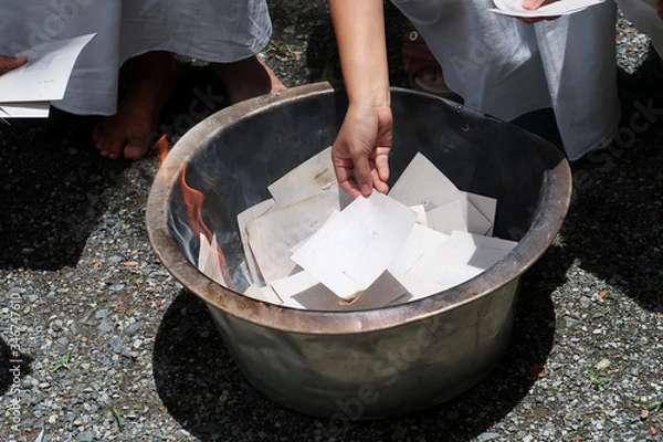 Obraz Woman hand putting  silver & gold paper on burning fire frame to make merit for dead person in funeral ceremony at Buddhist temple with traditional white cloths        