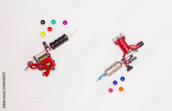 Obraz Rotary and induction tattoo machines and color paints in disposable plastic jars on a white background. Free space for text. The view from the top.