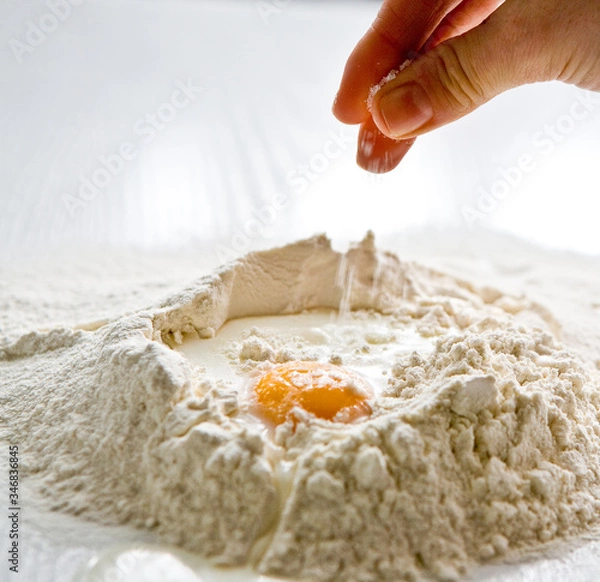 Fototapeta Adding salt to the heap of flour with egg for cooking