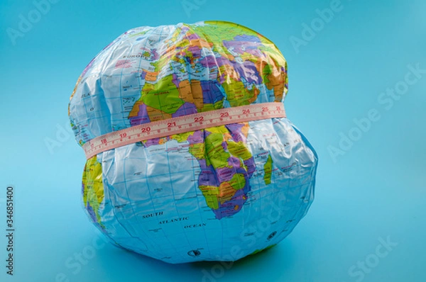 Fototapeta Global obesity epidemic crisis affecting increasing numbers of earth population and chronic health condition concept with globe and measuring tape isolated on blue background