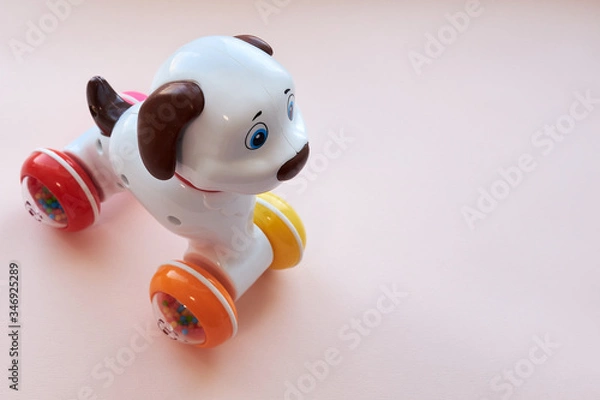 Fototapeta Children's toy from plastic a white dog with brown ears and a tail, on wheels on a pink background. Flat lay. Copy space.