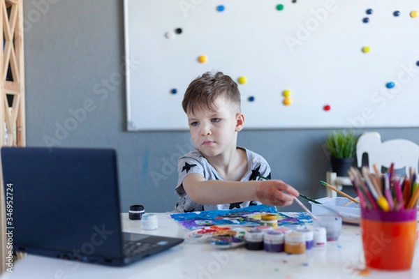 Fototapeta boy paints, online drawing classes, gray Tshirt with stars, laptop on the table