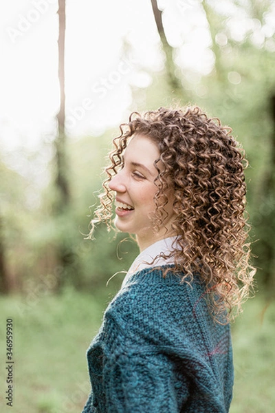 Fototapeta Portrait of laughing and smiling girl with curly hair on green and wooden background