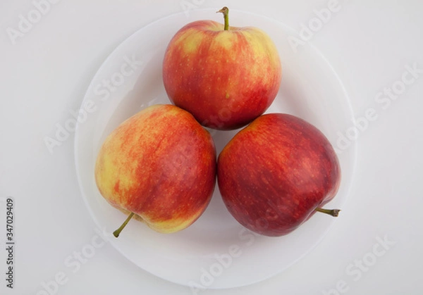 Fototapeta three red apples lie on a white plate on a white isolated background
