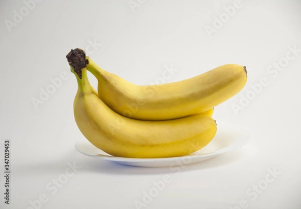 Obraz group of yellow bananas lies on a white plate on a white isolated background