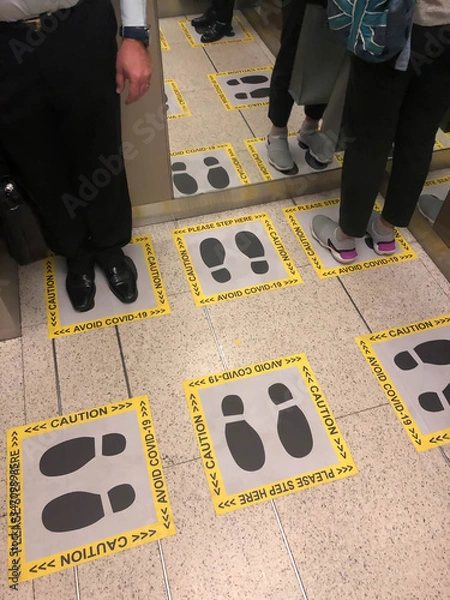 Fototapeta People in the elevator in the building standing in distance following with the footprint sign for the standing position to avoid Covid-19
