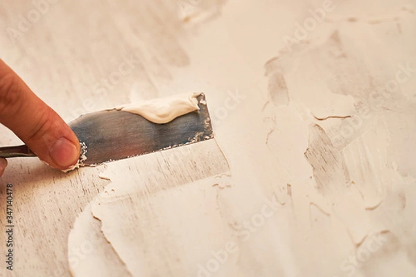 Fototapeta a small spatula applies putty to the wooden surface to create a structural background