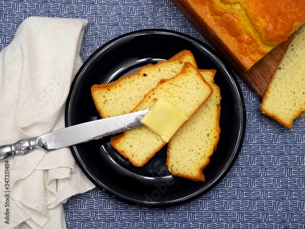 Obraz Fresh yellow cornbread out of the oven sliced and served with butter on a knife sitting on a navy blue plate and blue tablecloth.