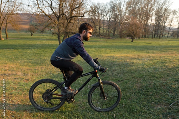 Fototapeta Cyclist in shorts and jersey on a modern carbon hardtail bike with an air suspension fork standing on a cliff against the background of fresh green spring forest