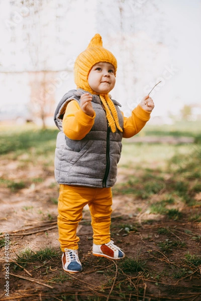 Obraz Stylish little one-year-old boy in a yellow hat, yellow pants and a gray jelly