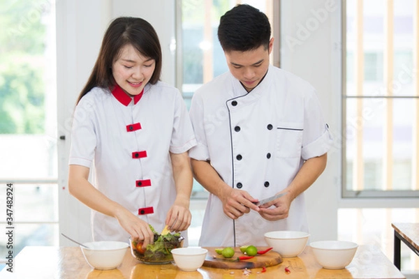 Fototapeta Two young Asian chefs helping each other Cook clean food with joy.