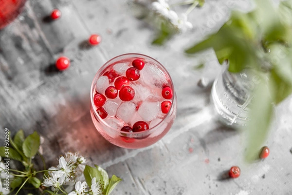 Fototapeta Top view spring cranberry lemonade in a glass on a gray shabby table with cherry flowers and leaves