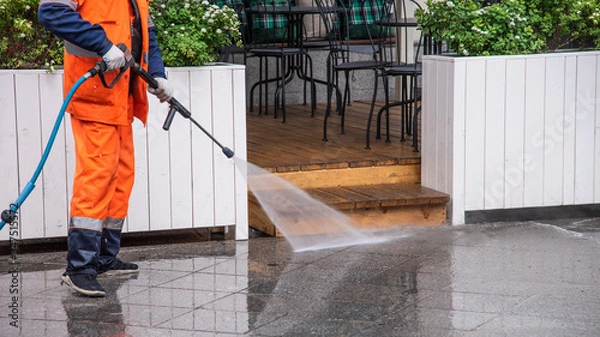 Obraz Worker washes the sidewalk in front of a street cafe - surface sanitation