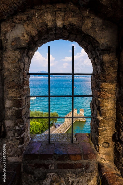 Obraz Sirmione seen through a grate window in the scaligero castel, a beautiful medieval picture of sea and land on the Garda Lake