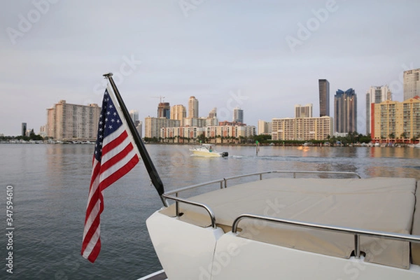 Fototapeta american flag on a yacht on the water against the background of skyscrapers in Miami