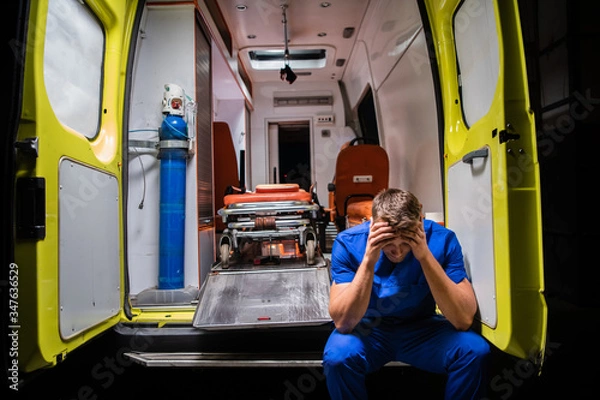 Fototapeta Confused paramedic in a blue uniform sitting in the back of an ambulance car