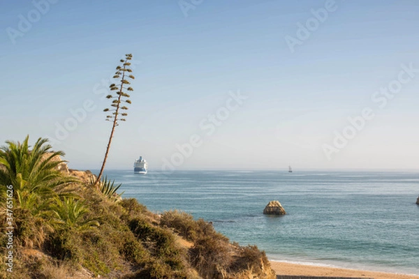 Obraz Big beautiful cruise ship at sunset in the ocean in the waters of Portugal in Europe. View from the cliffs of Praia da Rocha beach in Portimão, Algarve.