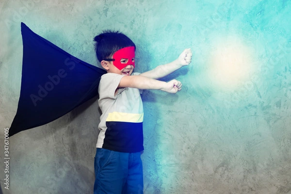 Obraz The boy dressed up in a superhero outfit, pretending to fight in studio,has light effect.Boy power concept And development of young children.