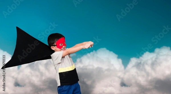 Obraz The boy dressed up in a superhero outfit, pretending to flying on the sky background.Study concepts And development of young children.