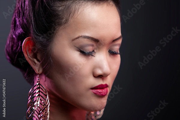Fototapeta portrait of a beautiful asian woman with gold earrings and red lips being happy and posing in isolated background. she long black hair and smooth clean skin