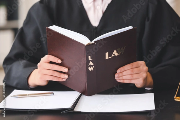Fototapeta Female judge with law book at table in office, closeup