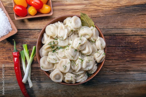 Fototapeta homemade dumplings with sour cream and dill on a wooden vintage table with fresh tomatoes, onions and spices