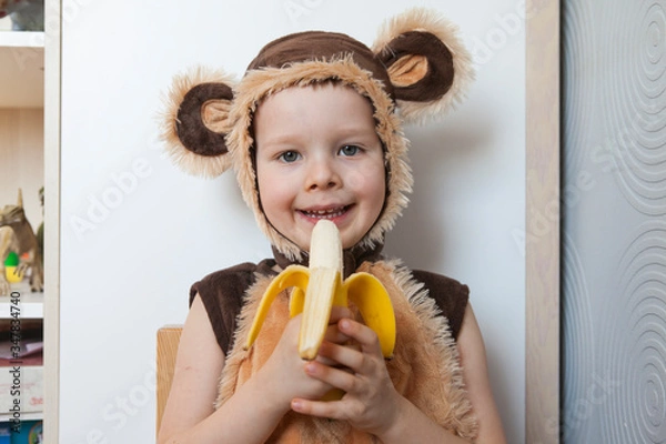 Obraz Image of cute toddler wearing a monkey costume, eating a banana