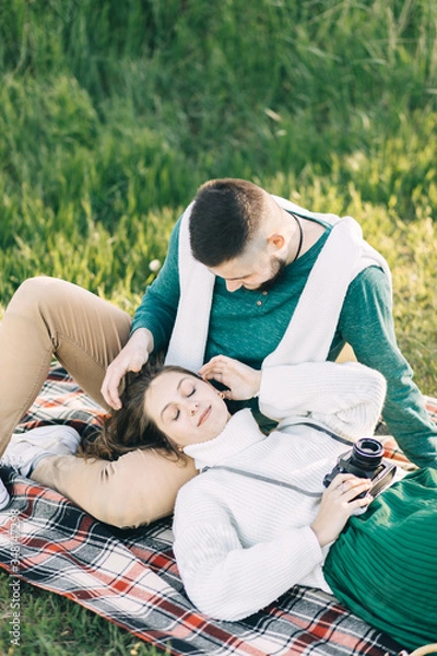 Fototapeta A guy and a girl love each other, smile, hug, kiss, laugh, enjoy life in the forest on a cliff, in the grass. Girl holding a film camera in her hands, photographs a guy, sunset in the background.
