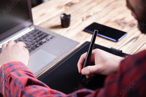 Obraz The workplace of the designer, men's hands work on a graphics tablet.