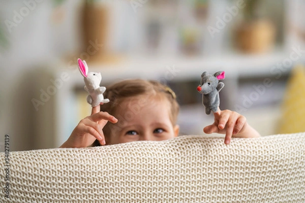 Fototapeta cheerful little girl is playing theater. Finger puppets are put on child's hands
