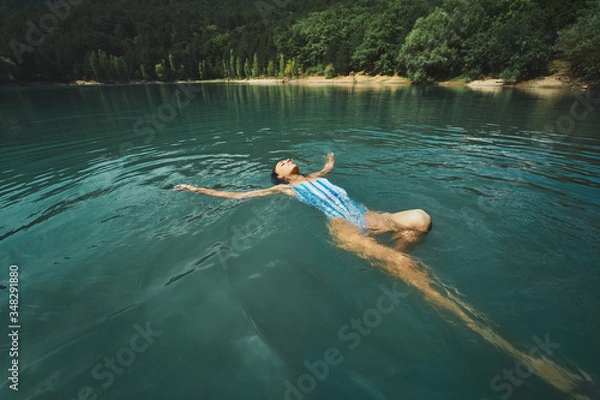 Obraz traveler carefree woman relaxing and floating in calm clear water, swimming on back in blue lake. Outdoor adventure, people in nature and calmness concept