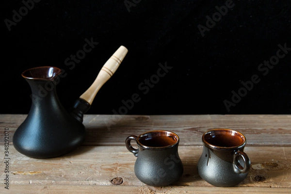 Fototapeta Two black cups for coffee and black turk on the old wooden table and black background. Cozy home idea. Sweet home