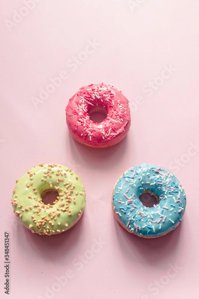 Fototapeta top view of assorted donuts of different colors such as pistachio, blue, pink and bilberry with frosted and filled with fruit cream and jam, colored glazed and sprinkled donuts on pink background