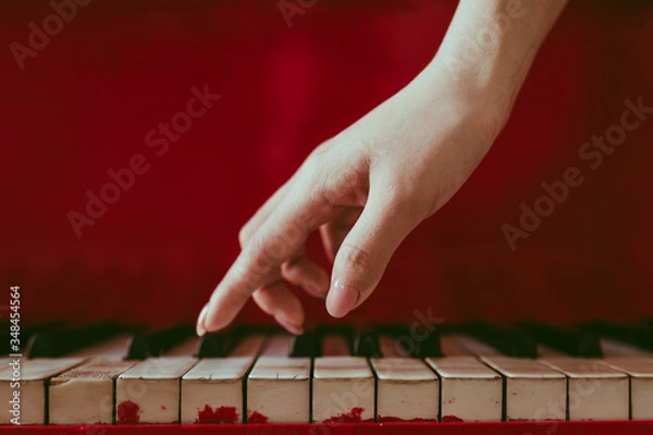 Fototapeta a close-up of a side view with female hand with pink manicure playing the piano. An old red piano with black and white keys. A palm above the keyboard. Graceful fingers of composer or musician