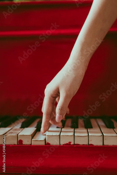 Fototapeta a close-up of a side view with female hand with pink manicure playing the piano. An old red piano with black and white keys. A palm above the keyboard. Graceful fingers of composer or musician