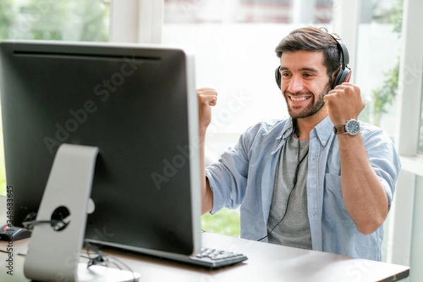 Fototapeta Handsome business man with casual cloth smile and express happy emotion look to monitor of computer in glass window room. He looks enjoy and relax during work from home in corona virus pandemic.
