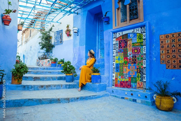Obraz Beautiful caucasian woman in a yellow dress and a boater hat posing in a blue city in Morocco. Chefchaouen.