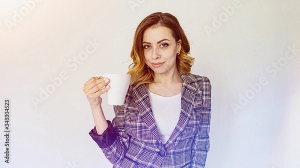 Fototapeta happy girl is standing with a cup of coffee and looking at the camera. beautiful girl in a checkered jacket is drinking coffee