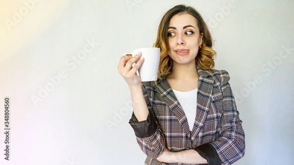 Fototapeta happy girl looks at a cup of coffee and licks her lip. beautiful girl in a checkered jacket is drinking coffee