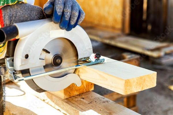 Fototapeta Manual circular circular saw on wood metabo. A man at a construction site saws a wooden Board bar close-up. The concept of working with wood on a sawmill. Woodworking equipment.