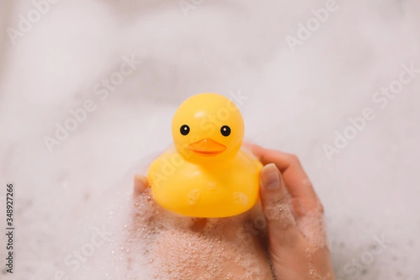 Obraz Girl is holding yellow rubber duck in the bath with bubble foam