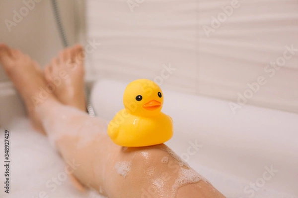 Obraz Girl is holding on her legs yellow rubber duck in the bath with bubble foam