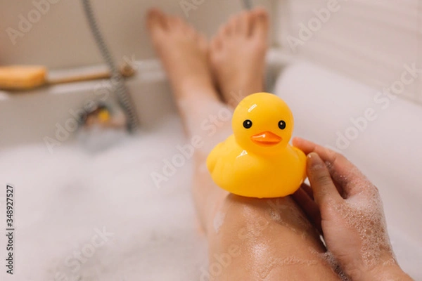 Obraz Girl is holding on her legs yellow rubber duck in the bath with bubble foam