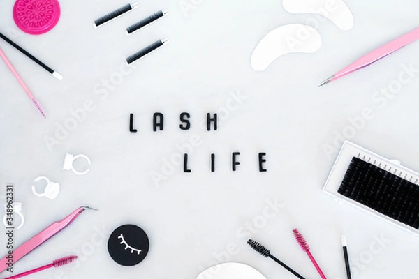 Fototapeta A beauty background displaying eyelash extension products, tools and equipment in a flat lay style.  The words lash life in the centre against a white background.