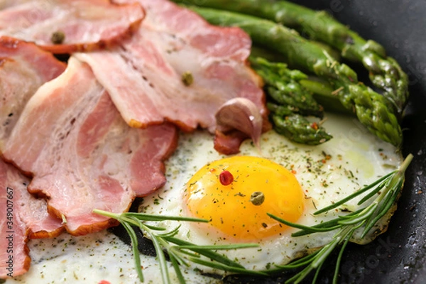 Fototapeta Fried asparagus with bacon, eggs and spices on a pan in close-up