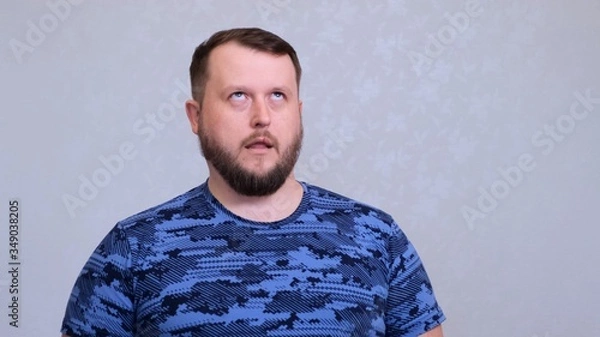 Fototapeta Tired fat bearded man in a blue T-shirt rolls his eyes. He was tired of work or tired of listening to his wifes conversation