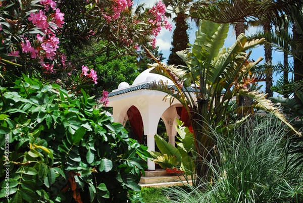 Fototapeta White arbor for relaxation in oriental style in dense thickets of tropical flowering plants