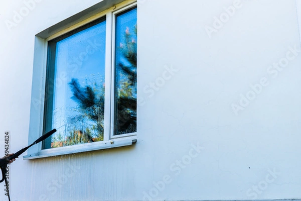Obraz Windows cleaning with a high-pressure sprayer.  The bright blue sky is reflected in the window